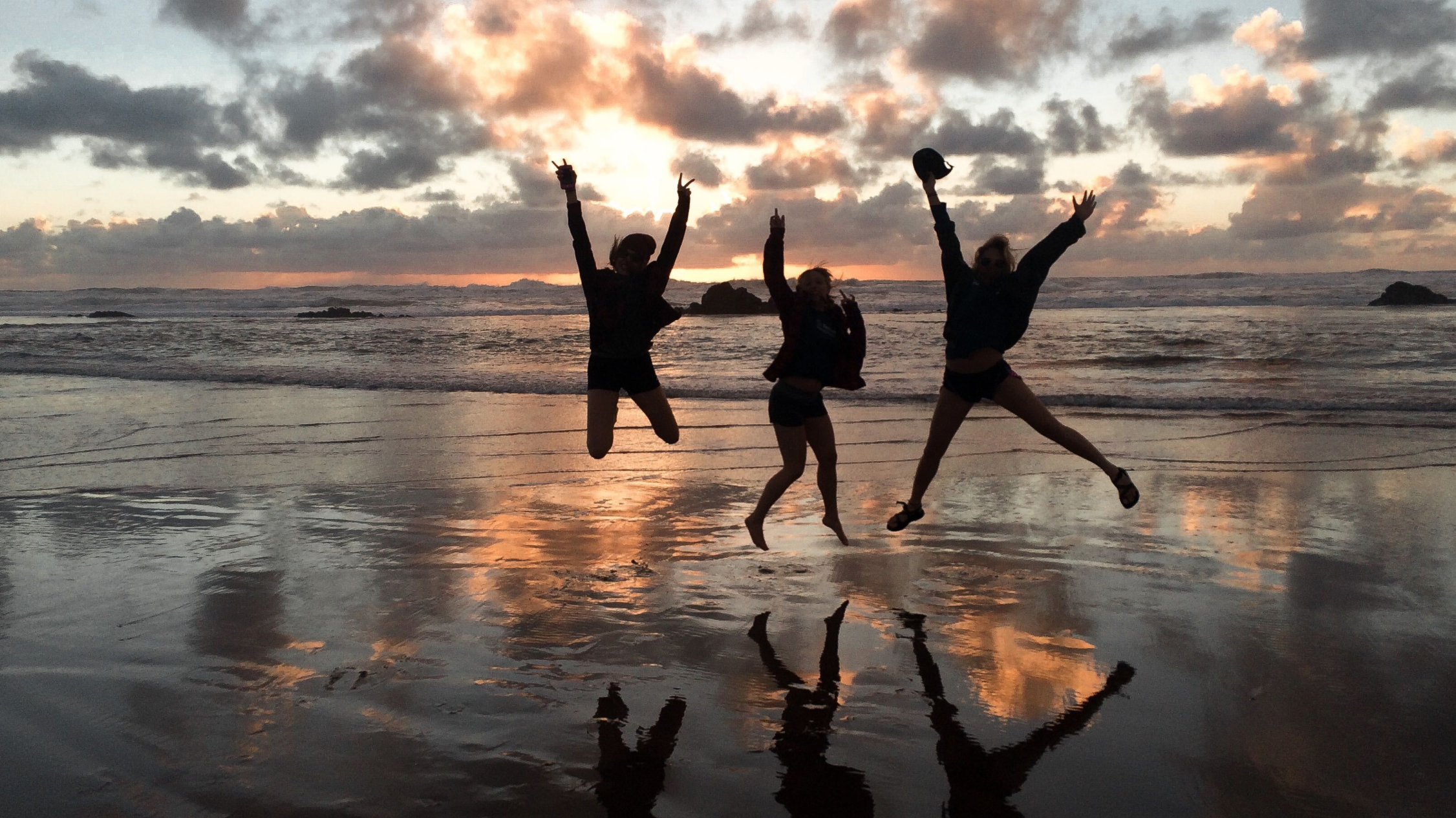 The silhouette of three people jumping for joy on the shore of a beach at sunset