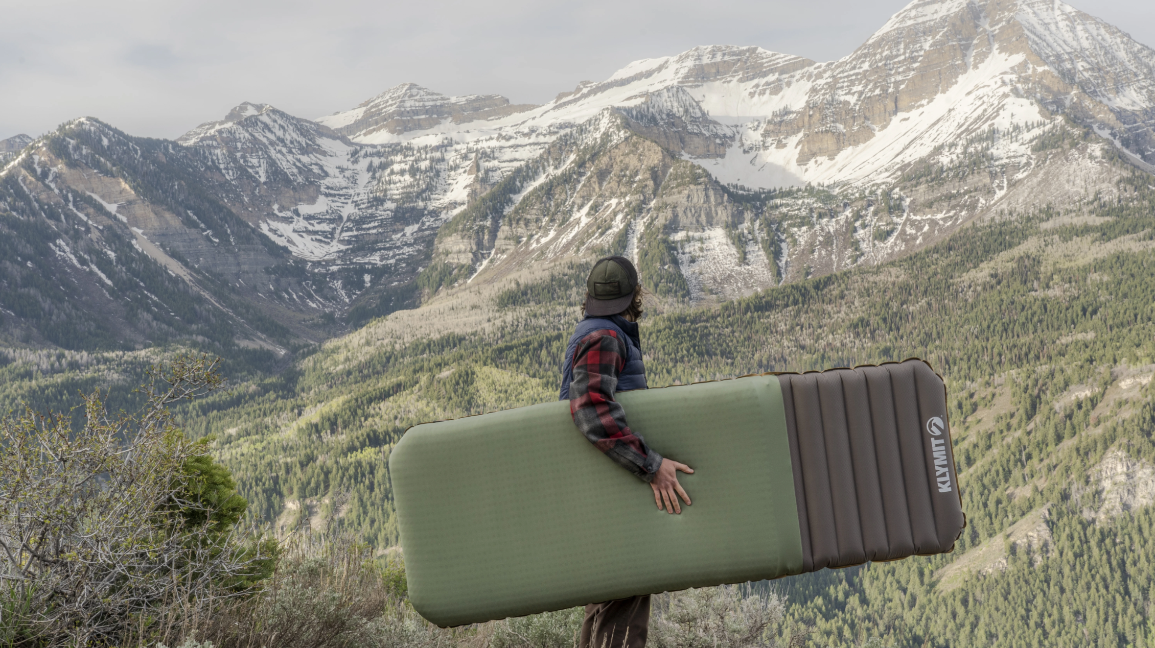 A person standing looking at mountains holding the Klmaloft sleeping pad