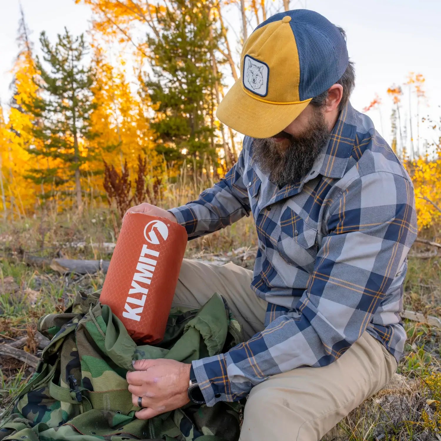Man taking out a red rock Klymit Insulated Static V Peak XL sleeping pad in its stuff sack from a backpack outdoors.