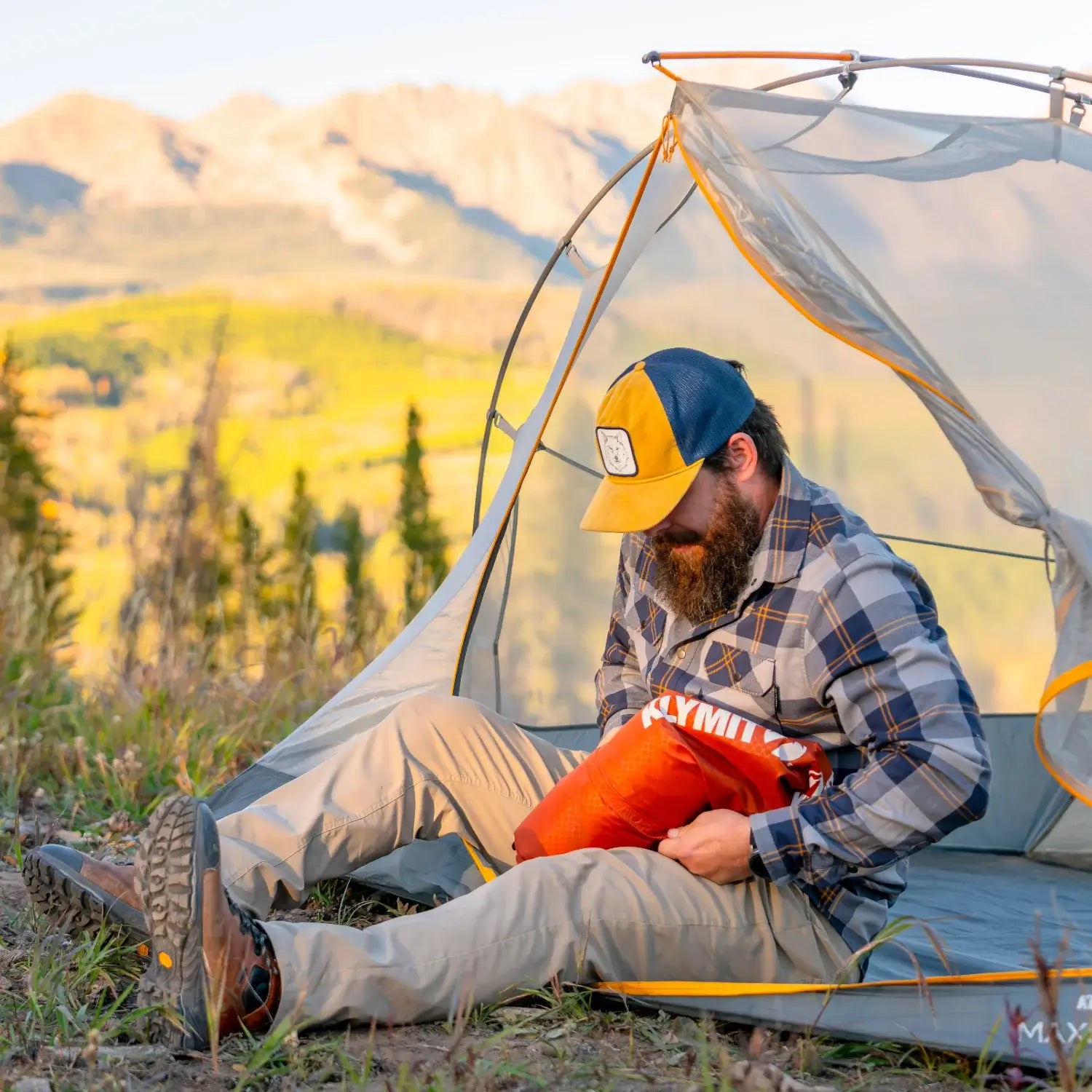 Man unpacking a red rock Klymit Insulated Static V Peak XL sleeping pad from a tent doorway.