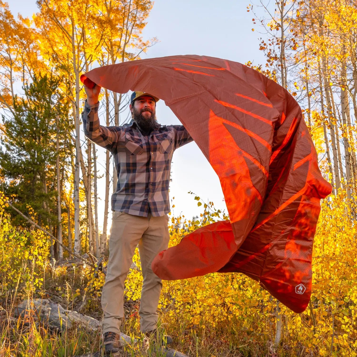 Man shaking out a red rock Klymit Insulated Static V Peak XL sleeping pad to inflate it outdoors.
