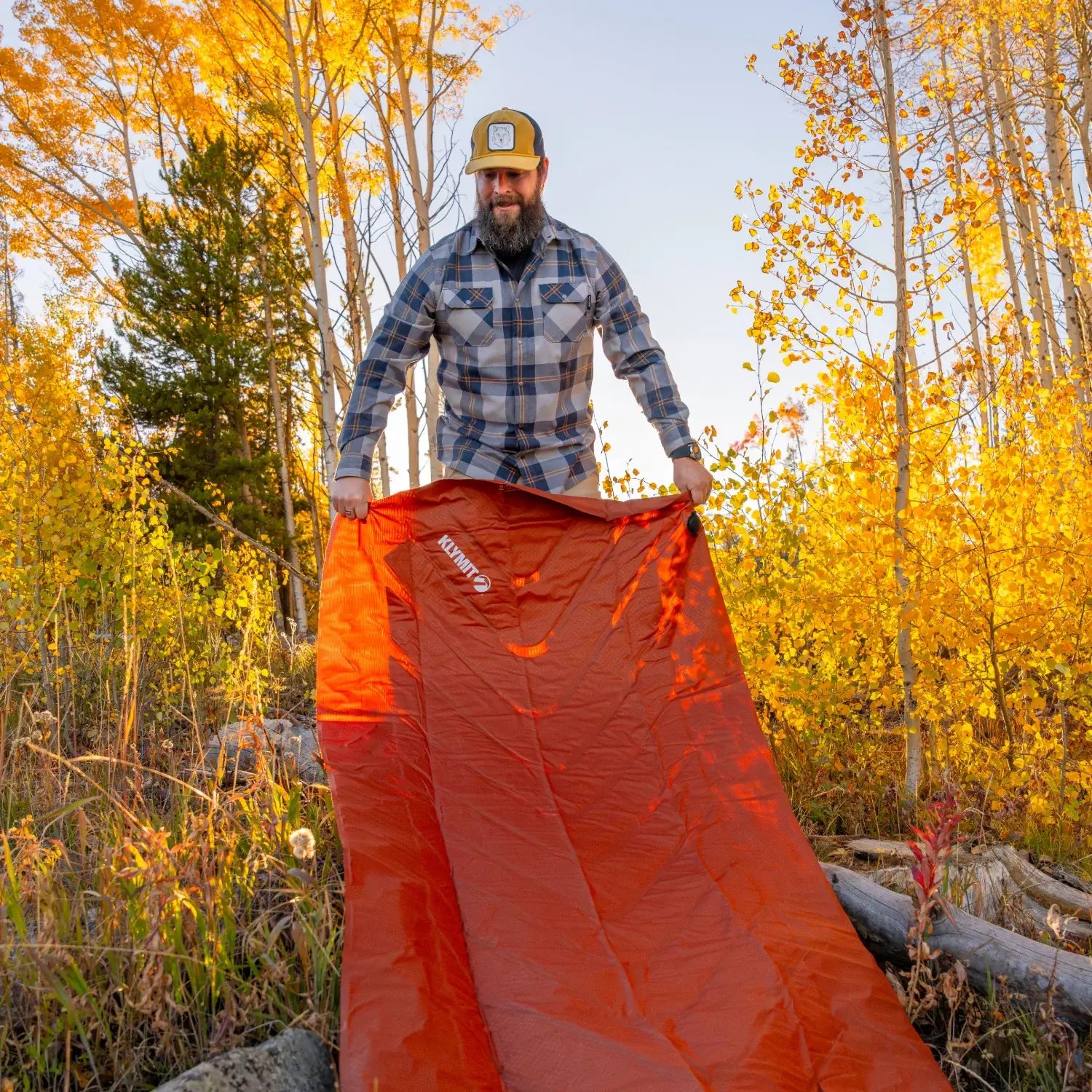 Man unfolding a red rock Klymit Insulated Static V Peak XL sleeping pad outdoors.