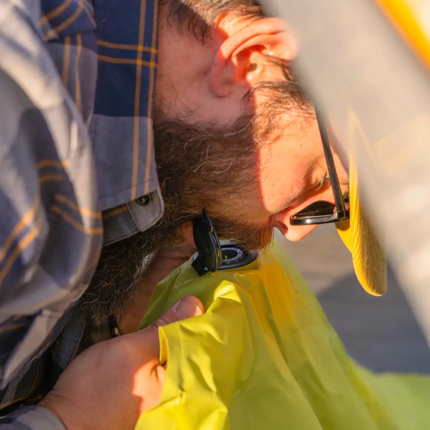 Close-up of a man inflating a chartreuse Klymit Static V Summit sleeping pad through its valve.