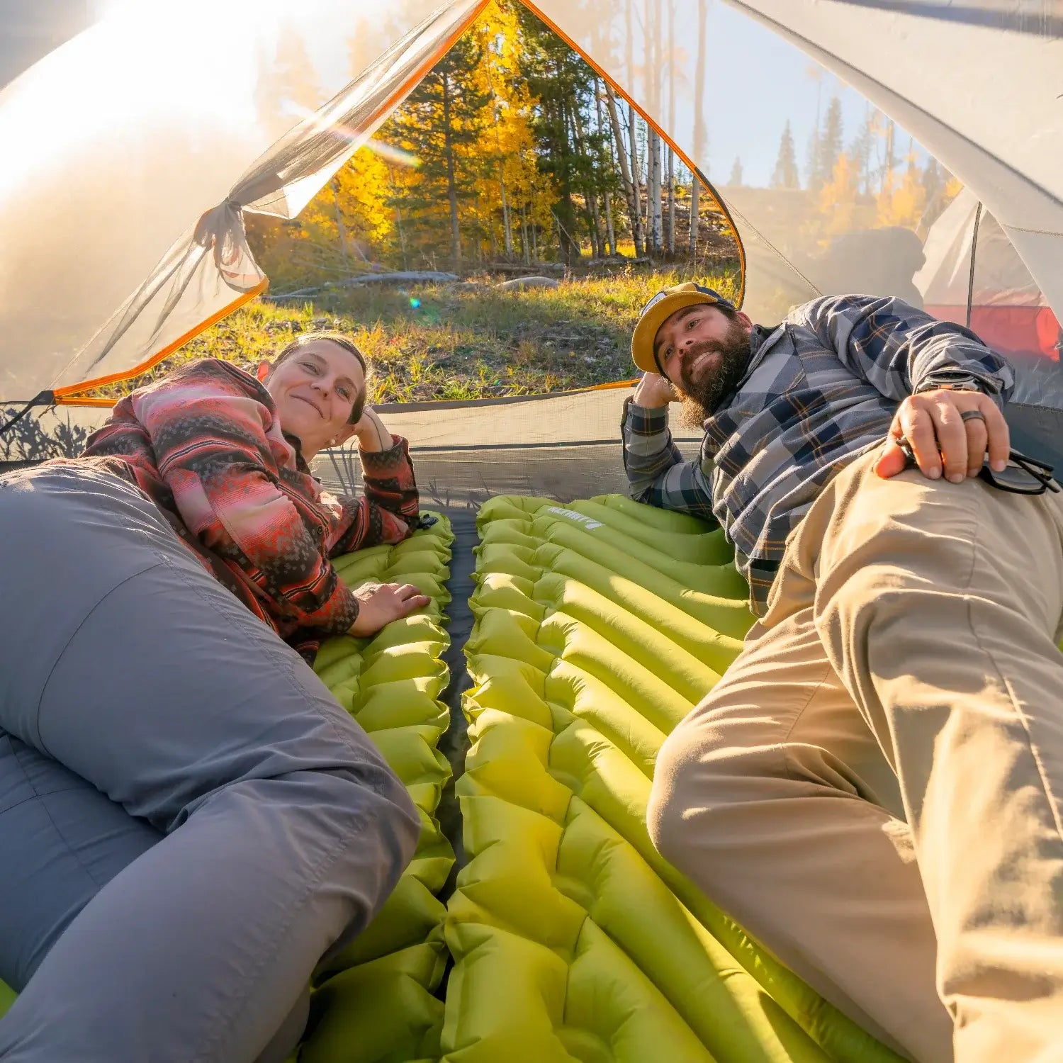 Couple lying on chartreuse Klymit Static V Summit sleeping pads inside a tent, smiling.