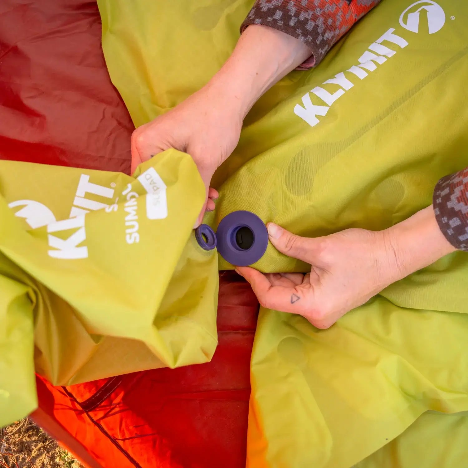 Overhead close-up of hands opening the valve of a chartreuse Klymit Static V Summit Double sleeping pad.