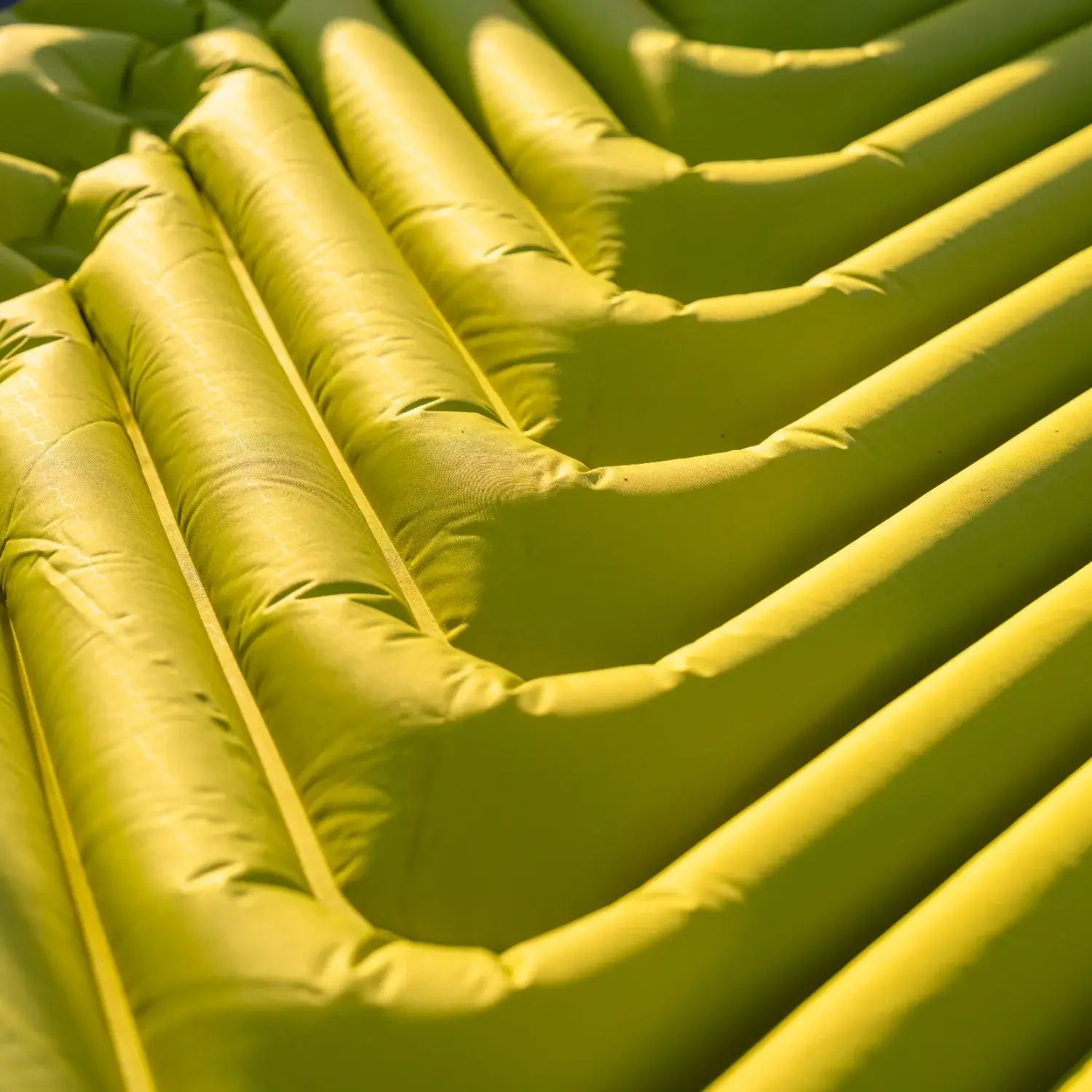 Detail shot of the chartreuse Klymit Static V Summit sleeping pad's V-shaped air chamber design in warm sunlight.