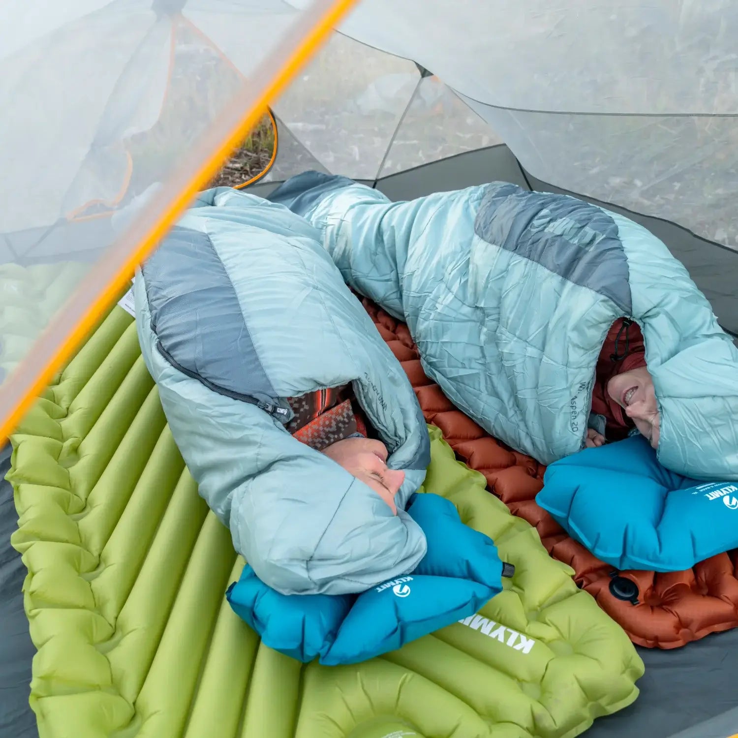 Overhead view of two campers in sleeping bags on Klymit Static V Summit sleeping pads in chartreuse and orange.