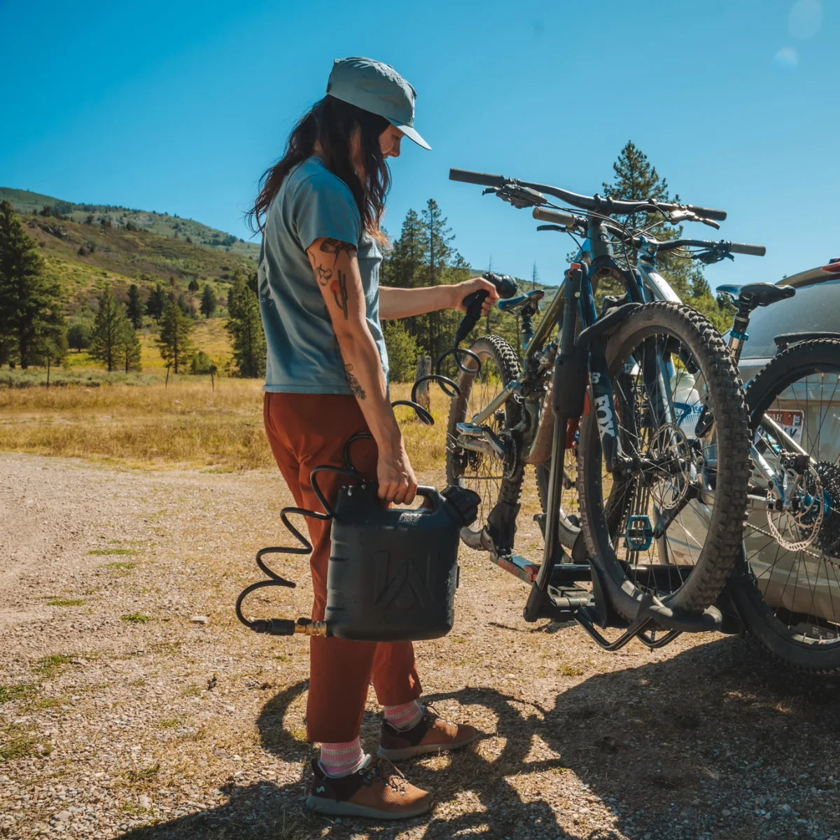 Cyclist spraying down a mountain bike with a Klymit WaterPORT GoSpout 2-gallon water tank at a trailhead.
