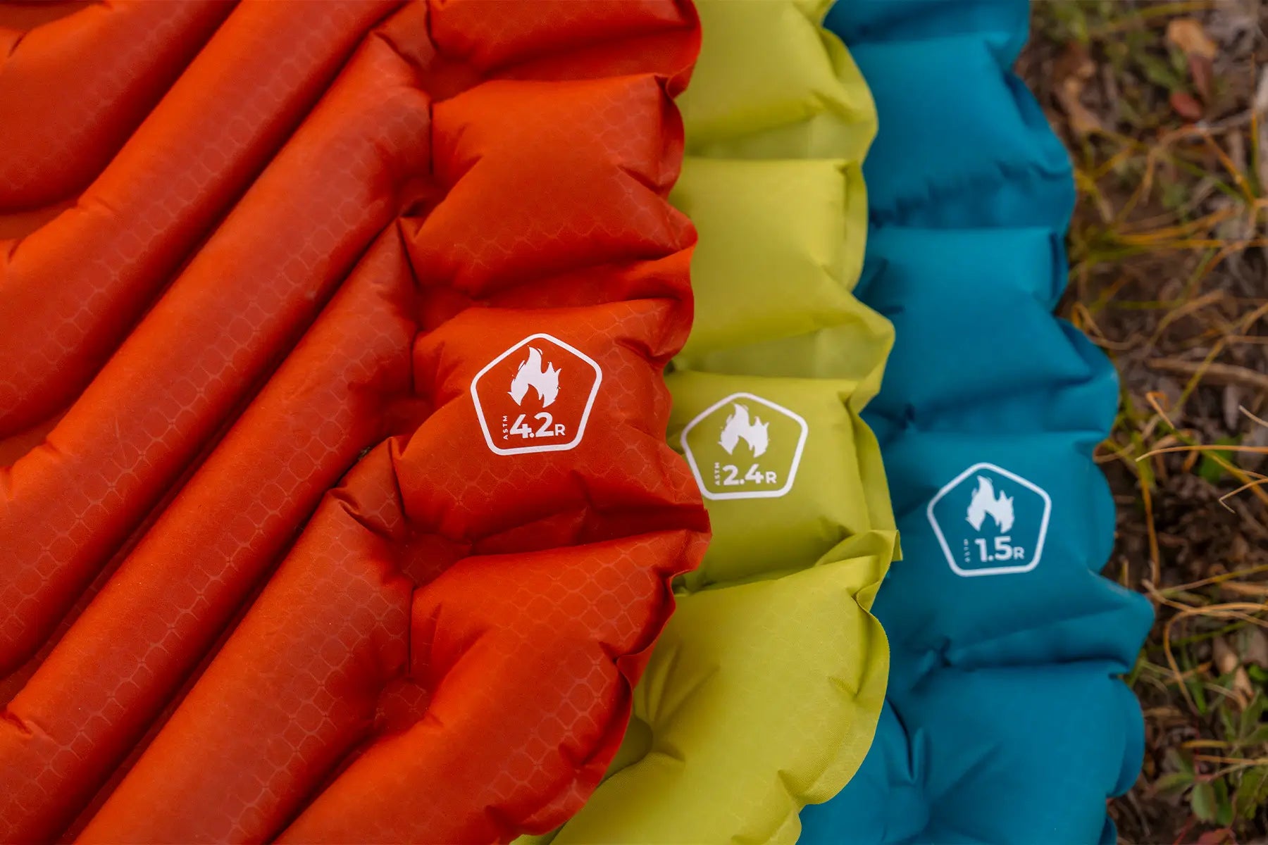 Close-up of three Klymit sleeping pads from the Peak, Summit, and Base series laid side by side, showing their R-value ratings of 4.2, 2.4, and 1.5.