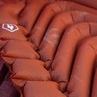 Close-up of the red rock Klymit Insulated Static V Peak sleeping pad's tubular air chambers showing texture and inflated structure.