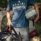 Wild Aspen 20 Degree Rectangle Sleeping Bag, Green, Lifestyle Man Carrying the Stuff Sack