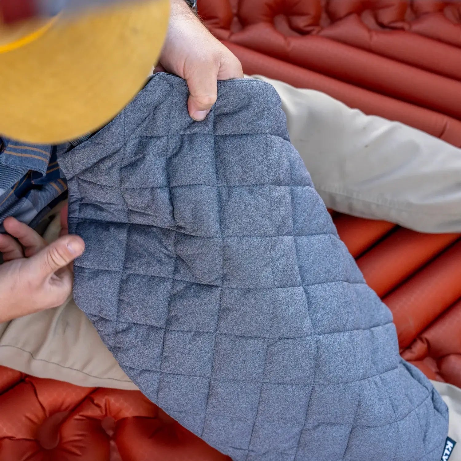 Close-up of a man holding an unfolded Klymit Pillow X Luxe Summit on a sleeping pad.
