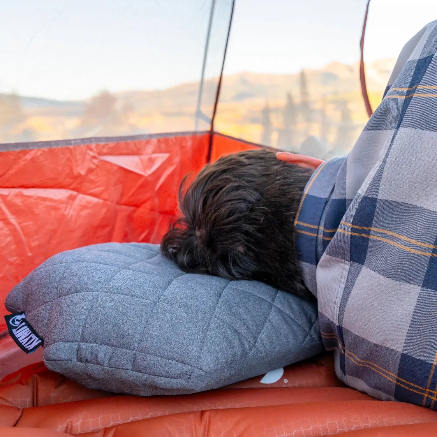 Man sleeping in a Klymit Pillow X Luxe Summit and sleeping bag inside a tent with a fall mountain view.