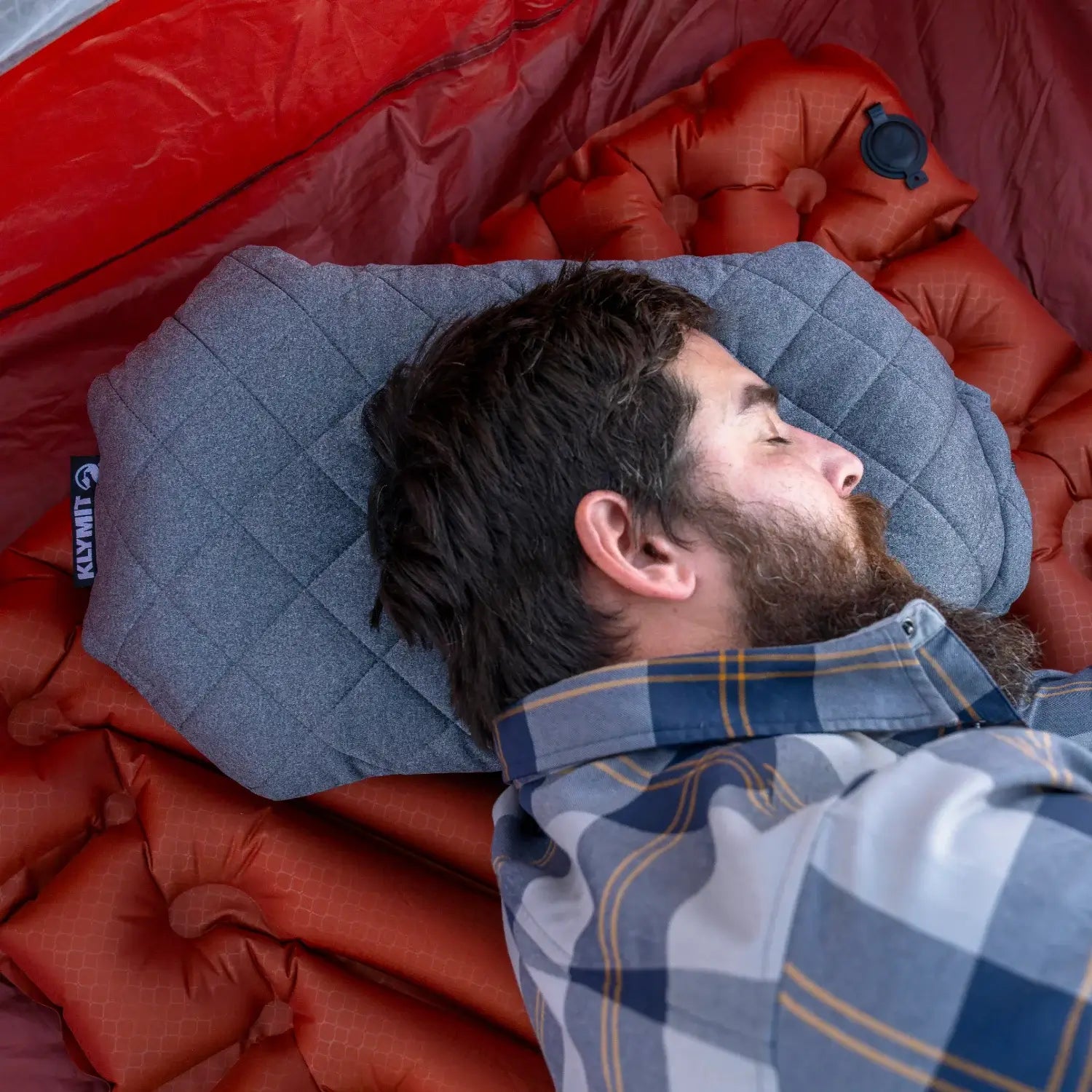 Overhead close-up of a man resting on a Klymit Pillow X Luxe Summit on a sleeping pad inside a tent.