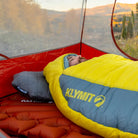 Man sleeping in a Klymit Pillow X Luxe Summit and sleeping bag inside a tent with a fall mountain view.