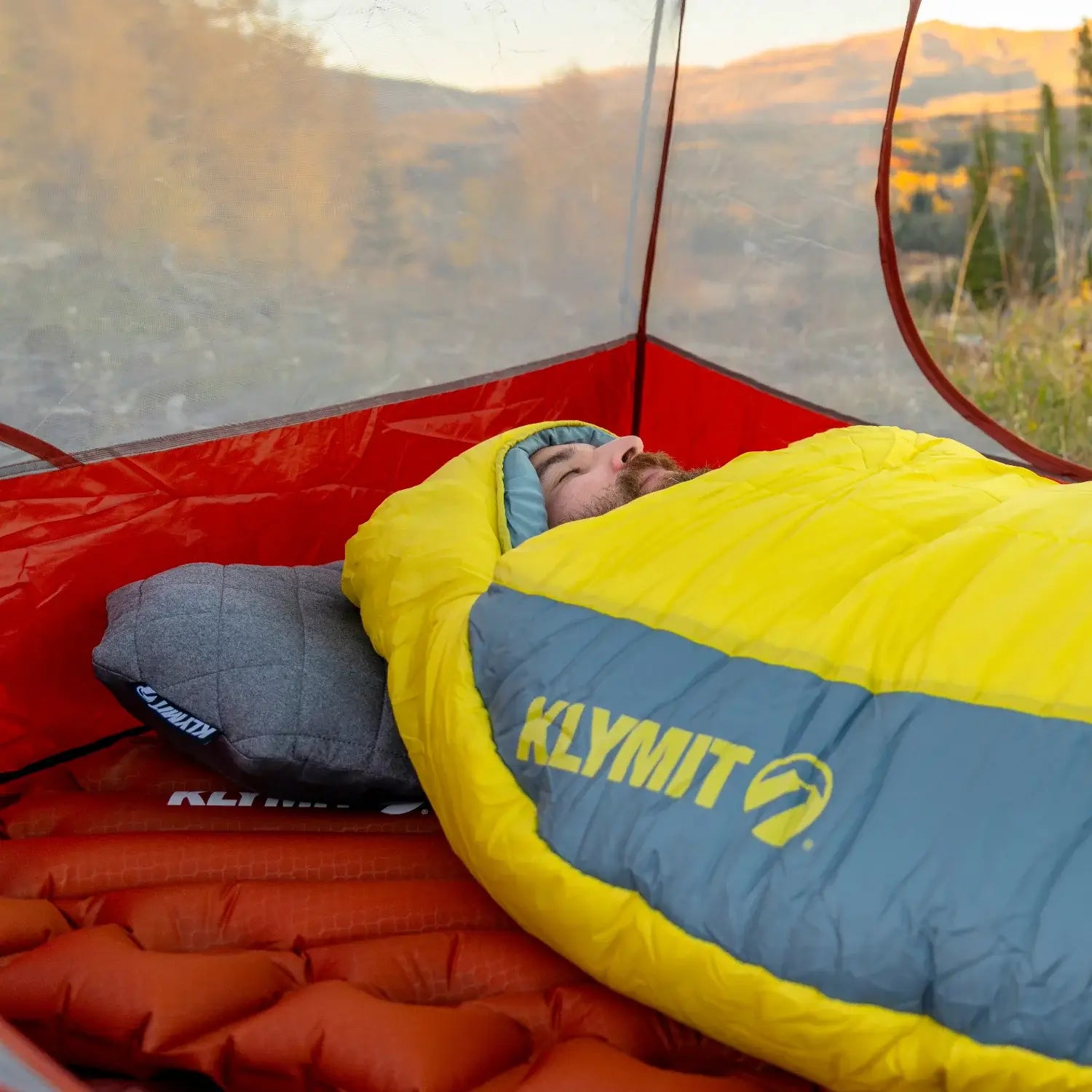 Man sleeping in a Klymit Pillow X Luxe Summit and sleeping bag inside a tent with a fall mountain view.