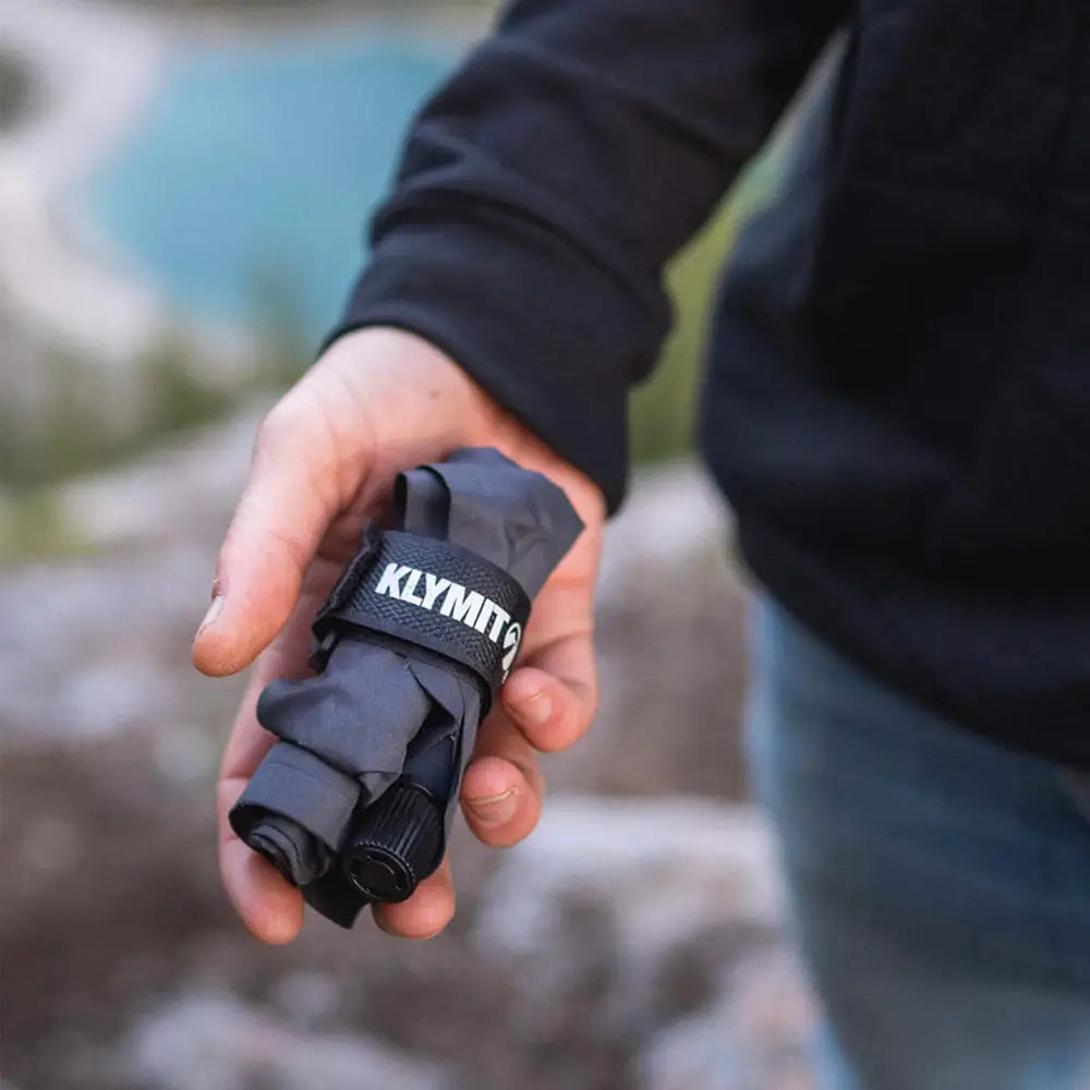 Hand holding a gray V-Seat with KLYMIT branding against a blurred natural background, all-groups
