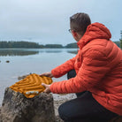 Person in an orange jacket setting up an orange V Seat by a lake.