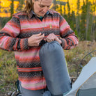 Woman packing a Klymit Wild Aspen 20 Regular sleeping bag into its stuff sack at a fall campsite.