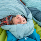 Overhead close-up of a woman tucked into a Klymit Wild Aspen 20 Regular sleeping bag on a Klymit sleeping pad.
