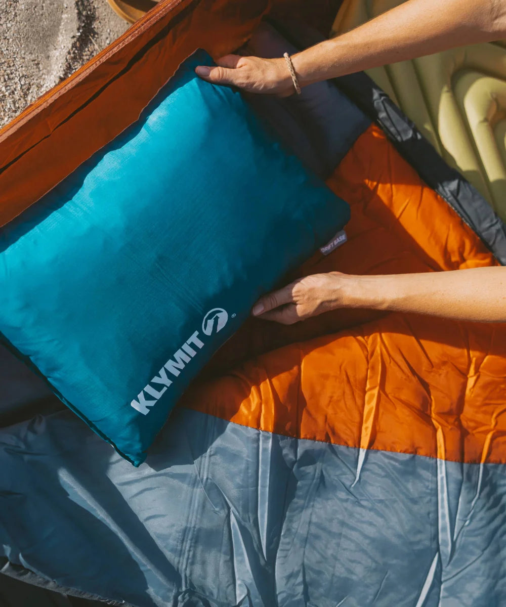 Hands set a Drift Base pillow inside a tent, next to a Bozeman 35 sleeping bag.
