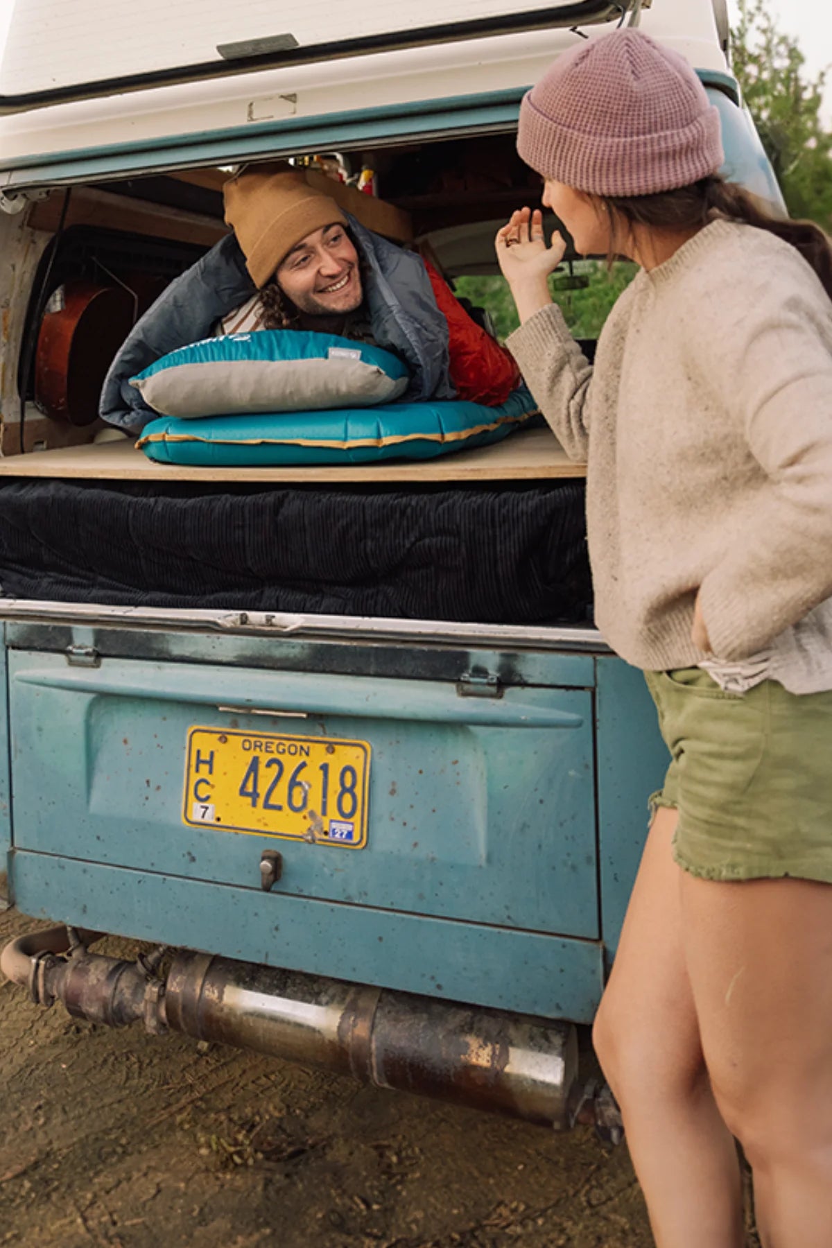 Couple sharing a moment at the back of their vintage camper van, featuring a sleeping pad and pillow from the Klymit Base series.