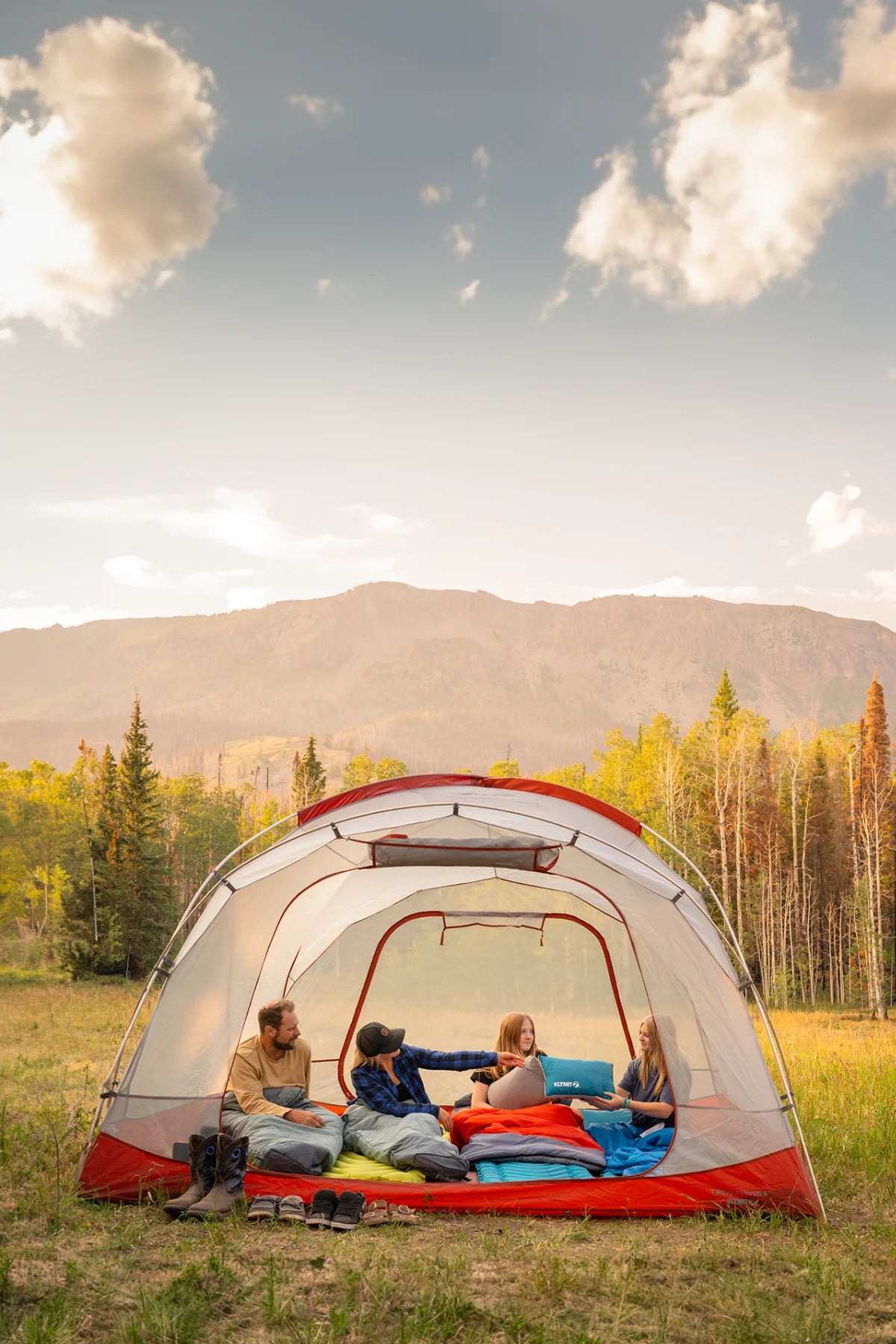 A family sits inside a tent on a lineup of Klymit sleeping pads, sleeping bags, and pillows.