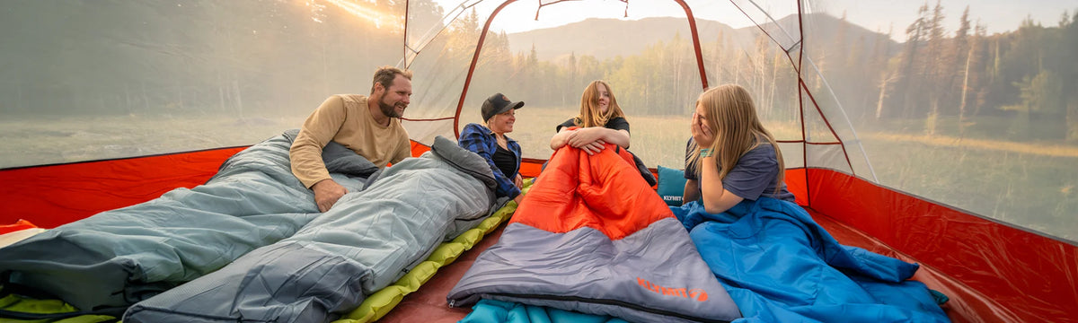 A family relaxes inside a tent on Static V Summit sleeping pads, Wild Aspen 20 sleeping bags, and a Bozeman 35 sleeping bag.