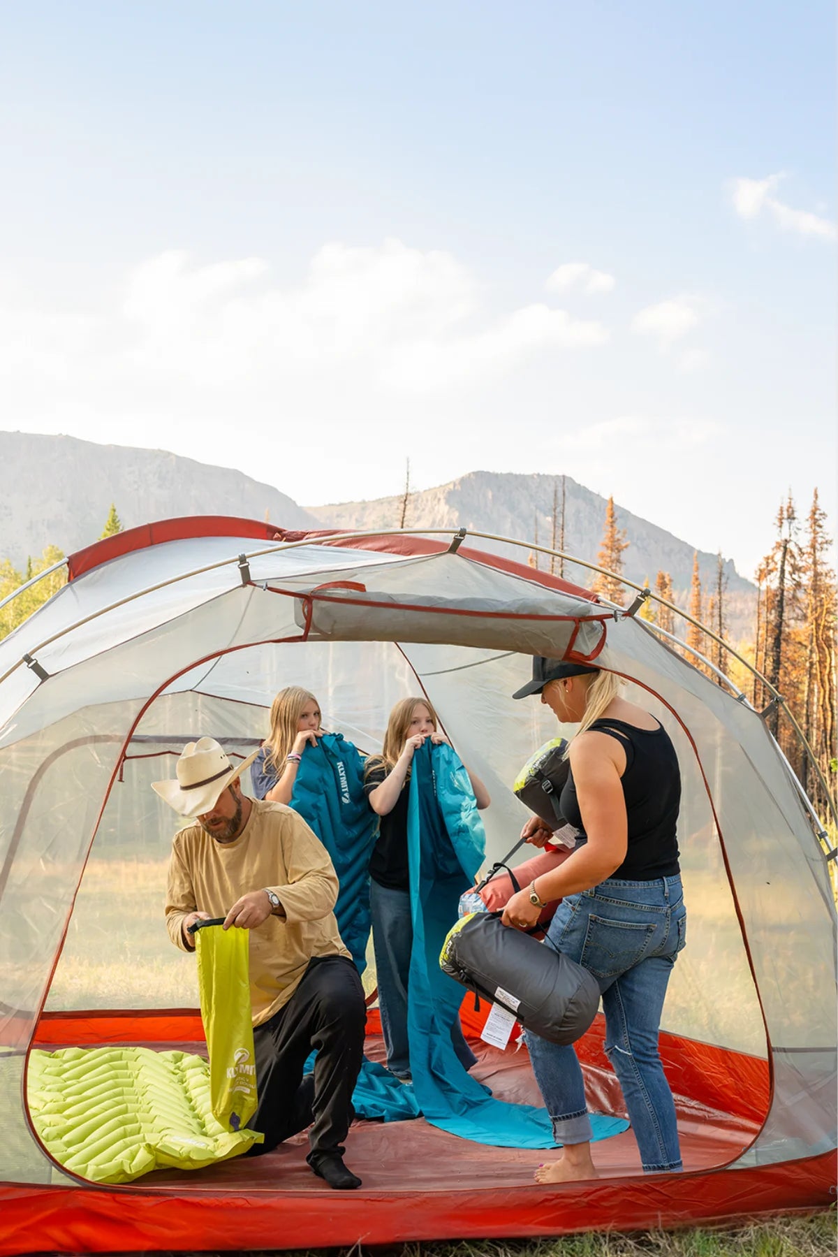 Family setting up Klymit sleeping pads and sleeping bags inside a large tent at a mountain campsite.