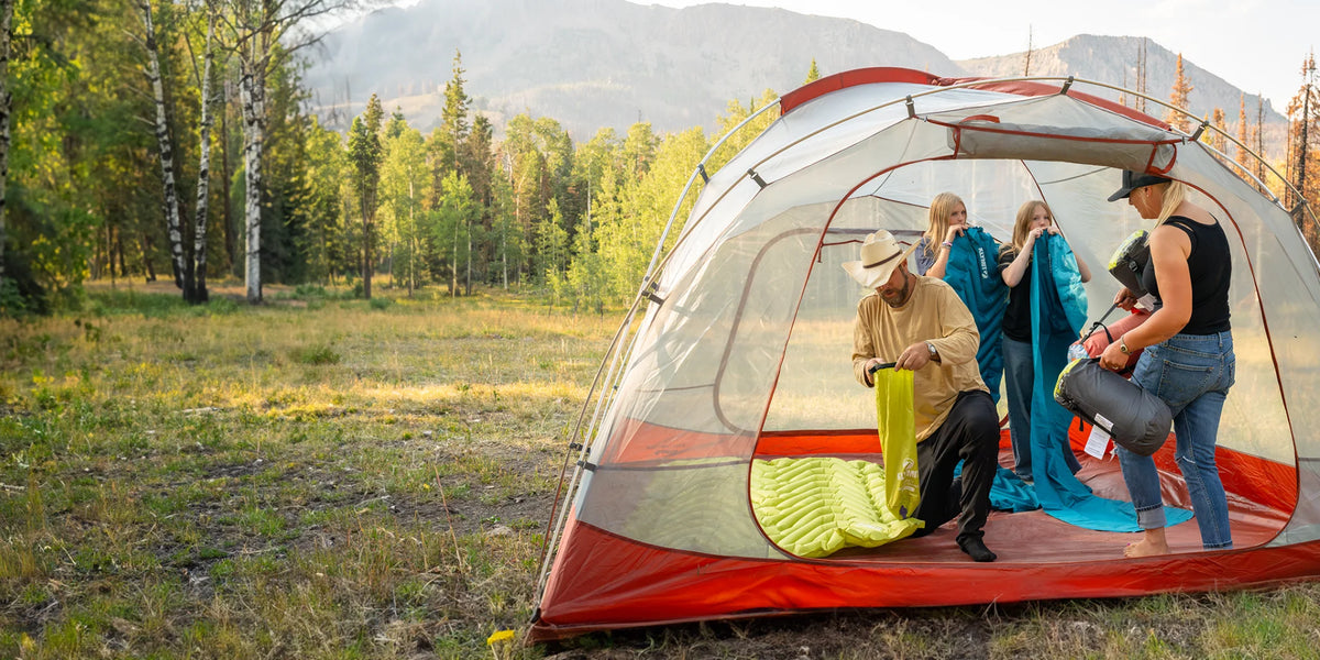 Family setting up Klymit sleeping pads and sleeping bags inside a large tent at a mountain campsite.