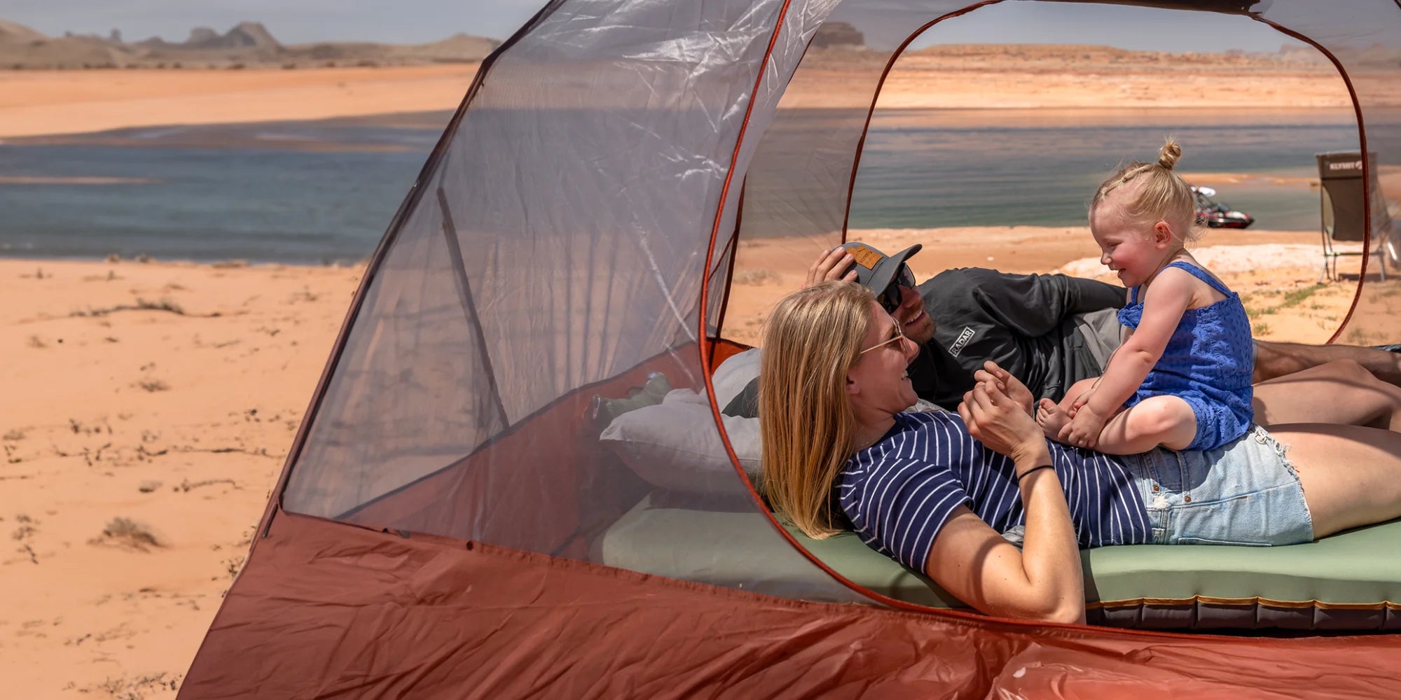 Family camping with Klymit Cross Canyon tent, Klymaloft Summit pad, and Drift Summit pillow at a lakeside desert campsite.