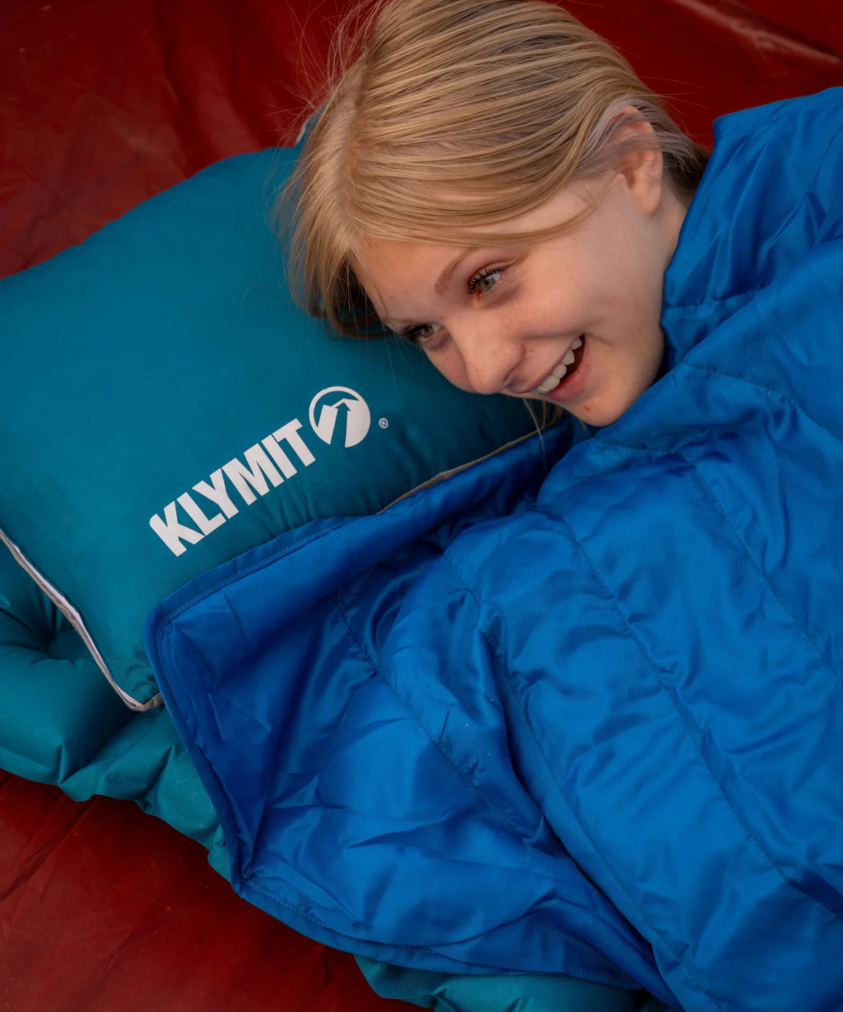 A girl rests her head on a Drift Base pillow, wrapped in a Horizon Travel Blanket.