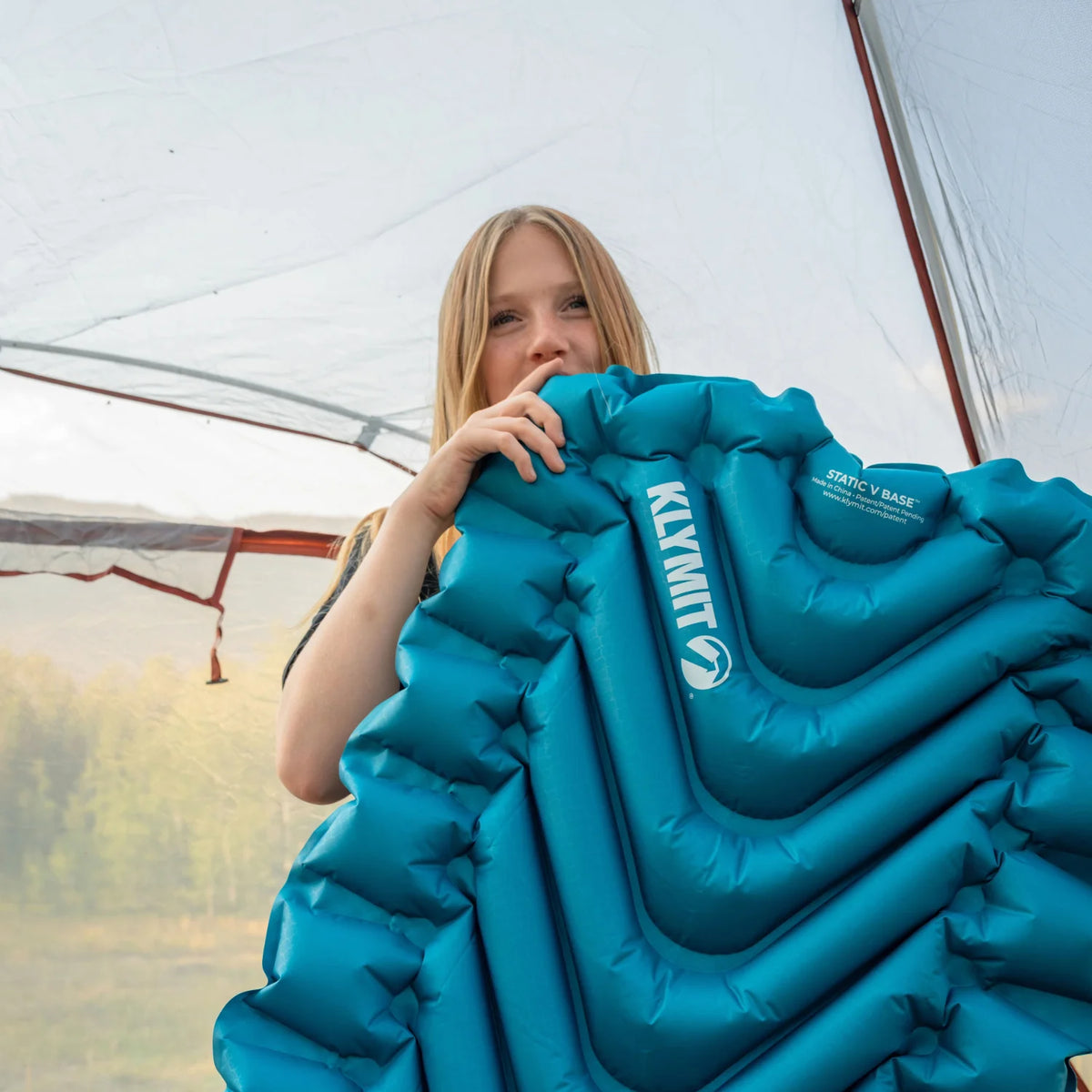 A girl holds up a Static V Base sleeping pad inside a tent.