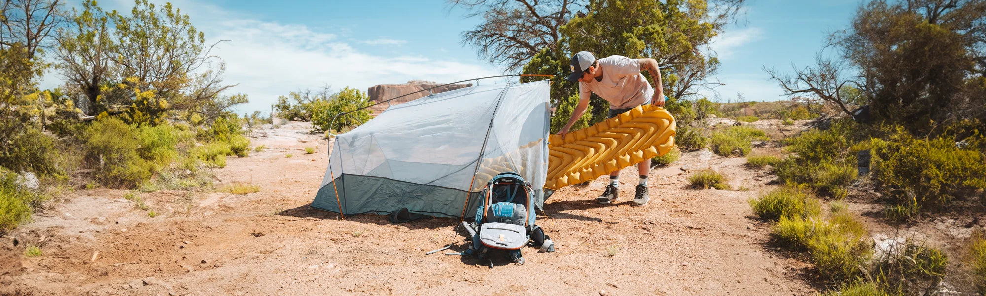 Man slides an inflated yellow Klymit Static V Lite Eco sleeping pad into a Maxfield tent pitched at a desert campsite.
