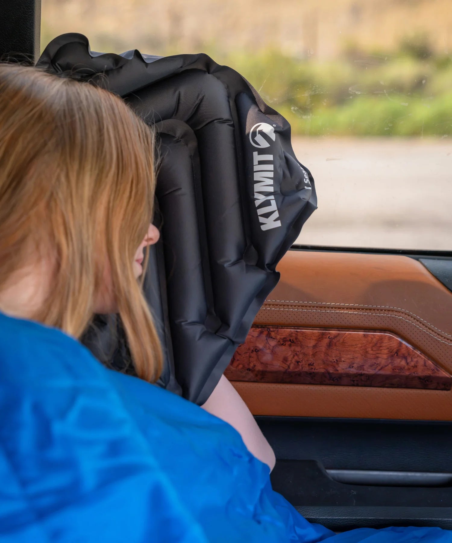 A girl rests their head against a V Seat  propped on a truck's window ledge.