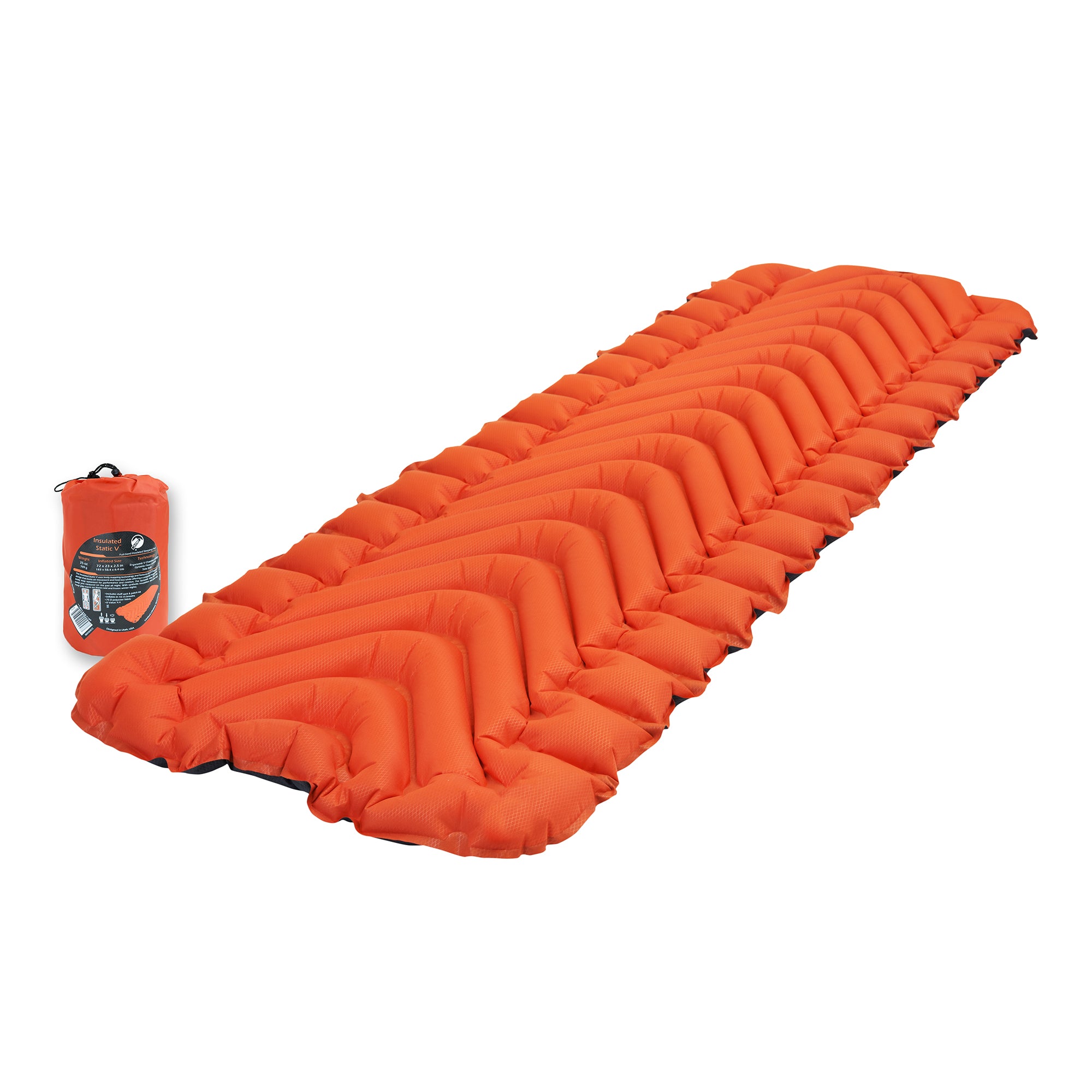 A rectangular orange inflatable sleeping pad with v shaped pattern shown at an angle on the ground next to its stuff sack.